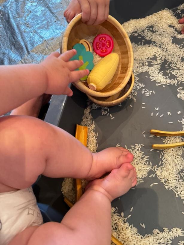 Bebê manipulando frutas de madeira em uma tigela durante a brincadeira