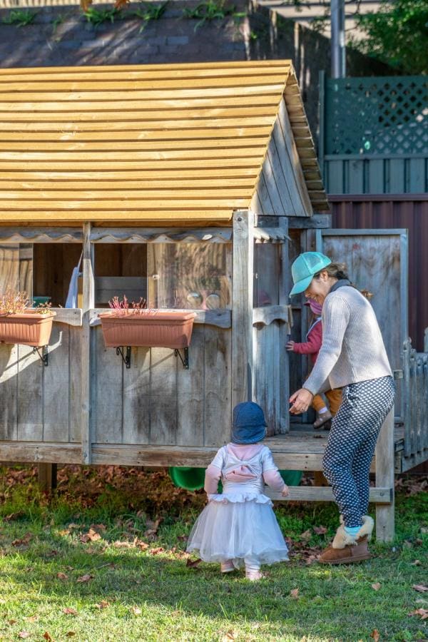 Educadora recebendo uma criança na casinha de madeira do quintal